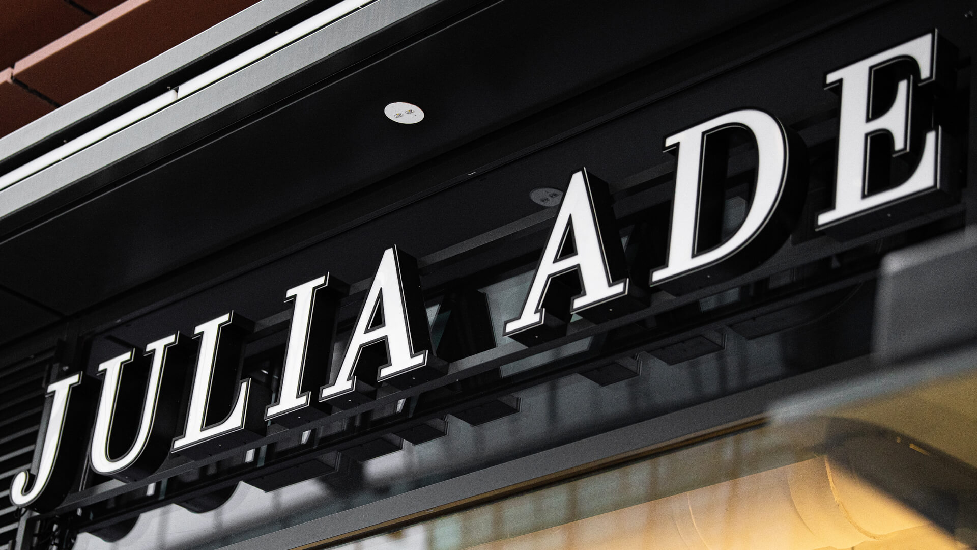 Julia Ade - 3D-Buchstaben, weiß beleuchtet, über dem Eingang.